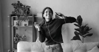 Eine Frau, die glücklich im Wohnzimmer tanzt und Musik hört
